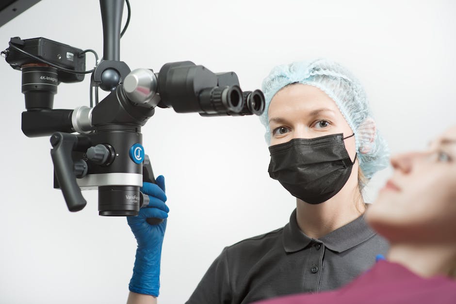 A dentist wearing protective gear examines a patient with a high-tech microscope.